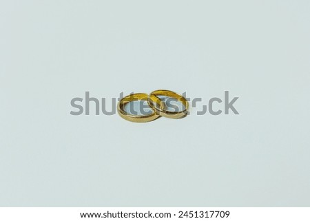 A close-up photo of two simple, elegant wedding rings resting side-by-side on a clean white background. The rings are made of gold and have a polished finish. Royalty-Free Stock Photo #2451317709