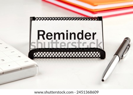 reminder word on a white business card next to a calculator, notepad and pen