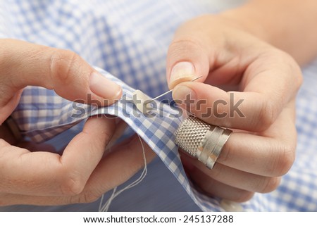 Closeup of woman hands sewing a button. Royalty-Free Stock Photo #245137288