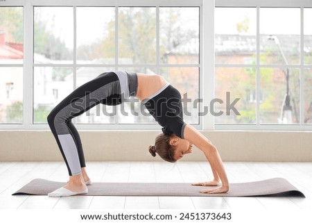 Sporty young woman doing yoga near window in gym