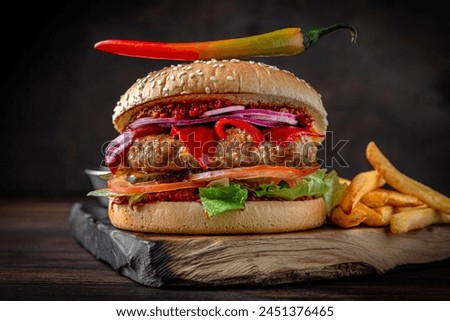 Spicy Burger with beef patty, hot peppers, cheese, vegetables and roasted potatoes. Juicy delicious hamburger on darkmood picture for restaurant decoration, poster. 