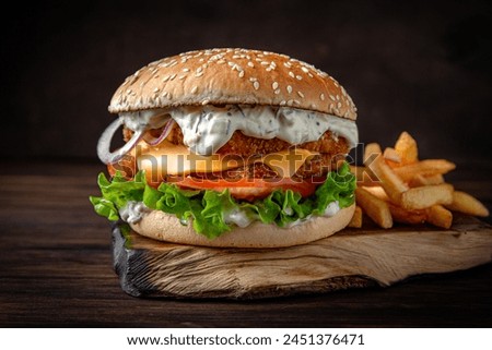 Fish burger with tartar sauce, cheese, vegetables, gravy and iceberg lettuce. Juicy delicious hamburger on darkmood picture for restaurant decoration, poster. 