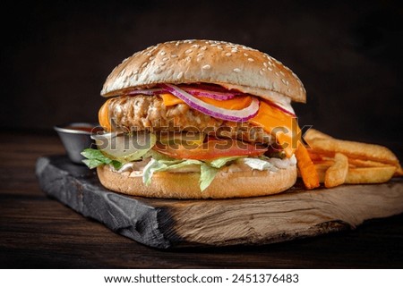 Burger with pork patty, cheese, vegetables and fried potatoes. Juicy delicious hamburger on darkmood picture for restaurant decoration, poster. 