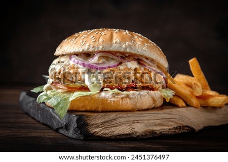 Burger with puffy patty, sheep and cow's milk based melted cheese, vegetables and fried potatoes. Juicy delicious hamburger on darkmood picture for restaurant decoration, poster. 