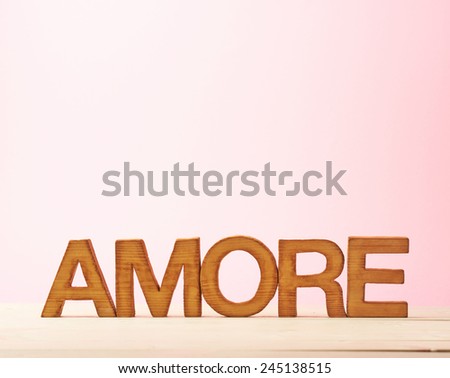 Word Amore meaning Love in Italian language as a composition of wooden block letters against the pink background