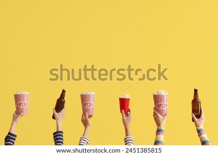 Many hands with buckets of popcorn and beer on yellow background