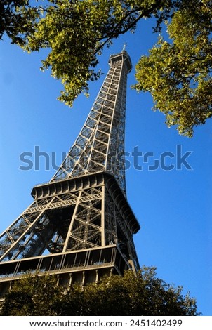 Closeup of the Eiffel tower of Paris in France among foliage on the blue sky background