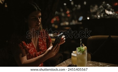 Beautiful hispanic woman captures fun nightlife moment, joyously tableside holding tropical cocktail drink at nightclub summer celebration