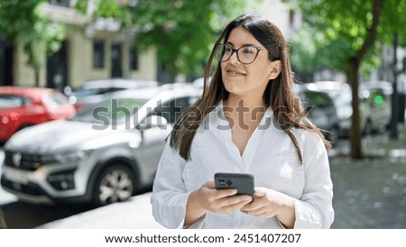 Young beautiful hispanic woman smiling happy using smartphone in the streets of Madrid