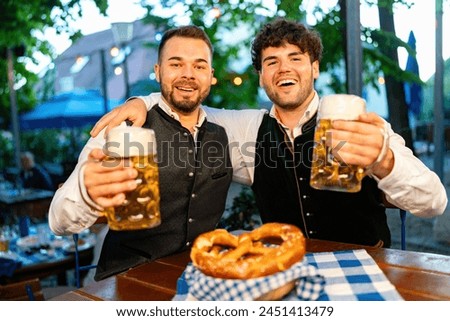 In Beer garden or Oktoberfest - Happy friends in Tracht, Dirndl and Lederhosen drinking fresh beer in mugs at Bavaria, Germany Royalty-Free Stock Photo #2451413479
