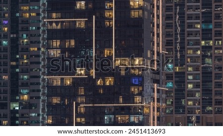 Rows of glowing windows with people in the interior of apartment buildings at night. Modern skyscrapers with glass surface. Concept for business and modern life. Tilt up