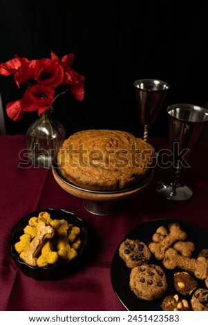 Still life in low key with a bouquet of poppies, homemade sponge cake, and dog bone-shaped cookies.