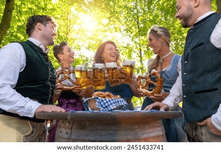 Waitress serving beer to a group of people in traditional tracht at oktoberfest or beer garden in germany Royalty-Free Stock Photo #2451433741