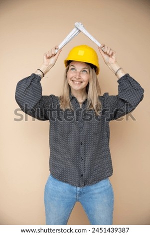 woman, architect, technician, builder, polisher with yellow safety hat and yellow folding rule in front of brown background Royalty-Free Stock Photo #2451439387