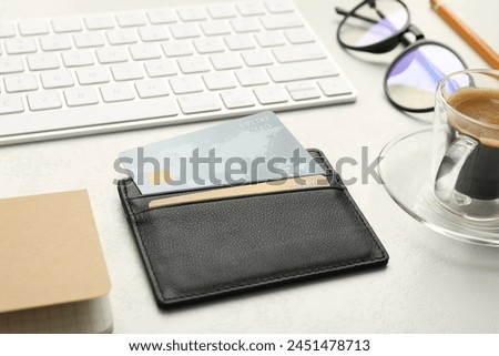 Leather card holder with credit cards, glasses, keyboard and coffee on white table, closeup