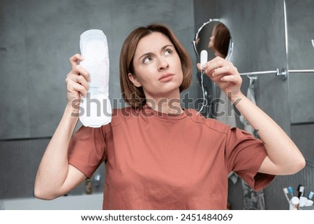 In a thoughtful moment, a woman contemplates her choice between pads and tampons, considering the comfort and convenience of each option Royalty-Free Stock Photo #2451484069