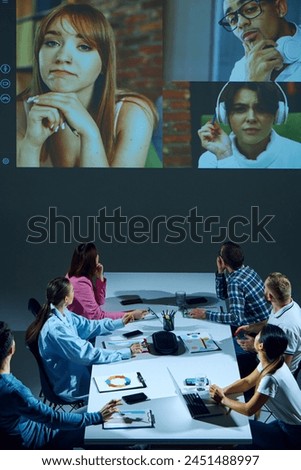 Colleagues in corporate environment participate in video conference call, sharing progress updates and addressing challenges with remote coworkers. Concept of business, communication, teamwork Royalty-Free Stock Photo #2451488997