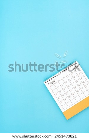 Desk calendar for August 2024 and white paper clip on a light blue color background