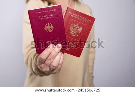 Close up of a woman in yellow sweater holding a German and a Russian passport, empty copy space background 