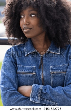A close-up portrays a Black woman with an afro, clad in a classic denim jacket, gazing away with a dreamy expression. The soft focus on her face enhances her contemplative look, suggesting deep