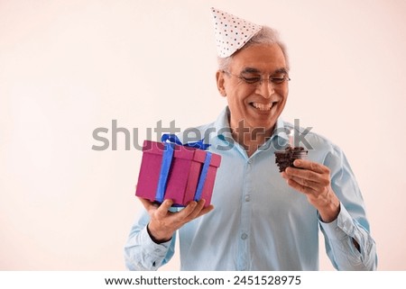Portrait of a happy senior man with holding birthday cake and gift in hands