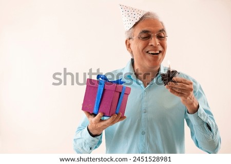 Portrait of a happy senior man with holding birthday cake and gift in hands