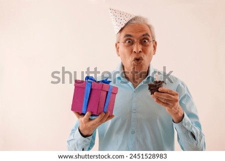 Portrait of a surprised senior man with holding birthday cake and gift in hands