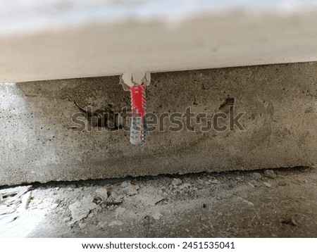 Red plastic anchors penetrate the seam, expanding to hold the anchors, blurred gray concrete background
