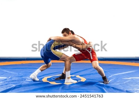 Two  strong men in blue and red wrestling tights are wrestling  on a white background. Wrestlers doing grapple. 