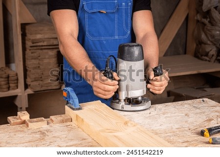close up of the an young  man wearing safety goggles carpenter builder pre-works the edges of the wooden board with a milling machine in the workshop, wooden sawdust flies to the sides