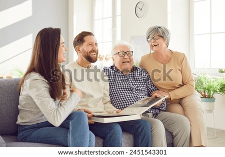 Happy family, aging old parents and adult children watching photo album to remember funny childhood memories, emotions. Home loving kind affection, trust, family care, peace over generations