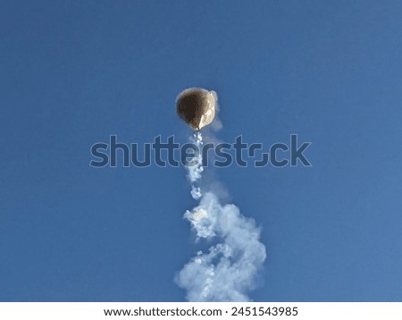 Photo of a hot air balloon carrying a series of firecrackers on its lower side tied with string and exploding while flying.