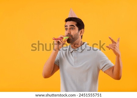 Happy young man blowing party horn and gesturing with fingers