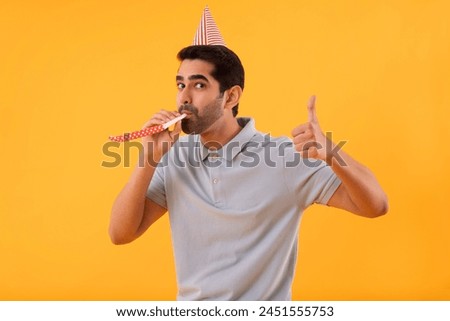 Happy young man blowing party horn and gesturing with thumb