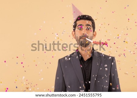 Happy business man in party hat blowing party horn while confetti falling on him