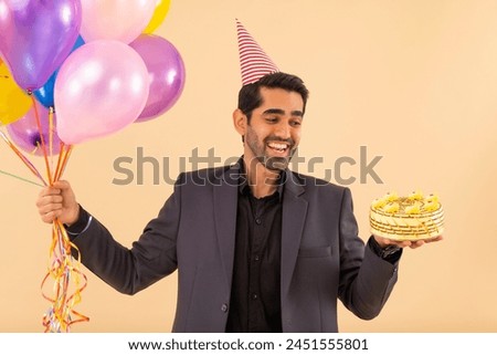 Happy business man holding balloons and birthday cake in hand