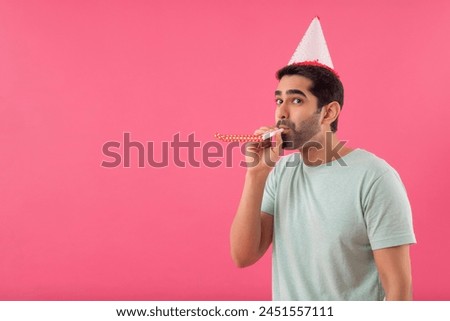 Happy young man wearing party hat and blowing party horn