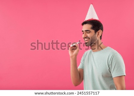 Happy young man wearing party hat and holding party horn in hand