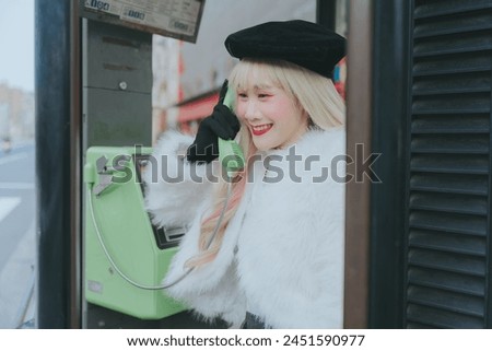 A woman wearing a beret and fur coat is talking on a payphone. Royalty-Free Stock Photo #2451590977