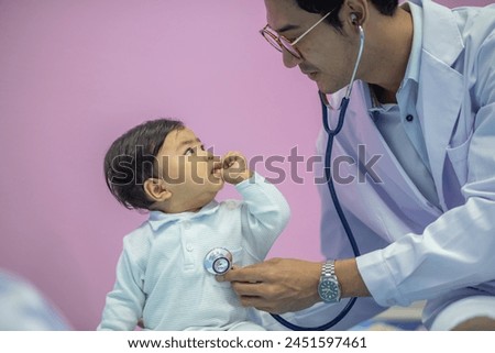 Mail pediatrician doctor in white cost gown hold stethoscope exam child infant patient. pediatrician sitting seduce misbehave baby infant for stethoscope checkup in hospital children medical care Royalty-Free Stock Photo #2451597461