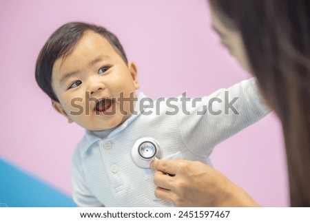 Woman pediatrician doctor in white cost gown hold stethoscope exam child infant patient. pediatrician sitting seduce misbehave baby infant for stethoscope checkup in hospital children medical care Royalty-Free Stock Photo #2451597467