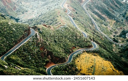 A picturesque asphalt road passing among mountains covered with tropical green forest on an island, a highway to a national park, a photo without people, a view from above.