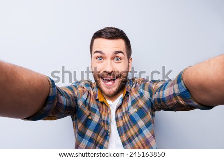 I love selfie! Handsome young man in shirt holding camera and making selfie and smiling while standing against grey background Royalty-Free Stock Photo #245163850
