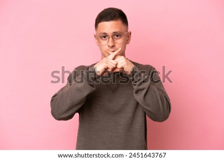 Young Brazilian man isolated on pink background showing a sign of silence gesture