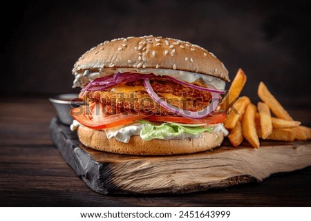 Burger with puffy chicken patty, cheese, iceberg lettuce. Juicy delicious hamburger on darkmood picture for restaurant decoration, poster. 
