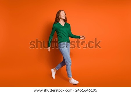 Full length photo of funky cheerful lady dressed green shirt walking empty space isolated orange color background