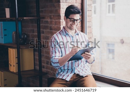 Photo of nice young corporate man pen write clipboard wear striped shirt loft interior office indoors