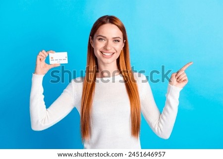 Photo portrait of attractive young woman hold credit card point empty space dressed stylish white clothes isolated on blue color background
