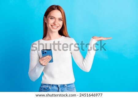Photo portrait of attractive young woman hold device palm hold empty space dressed stylish white clothes isolated on blue color background