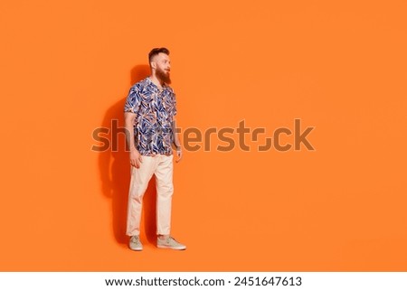 Full length photo of serious pleasant guy wear print shirt white trousers look at discount empty space isolated on orange color background